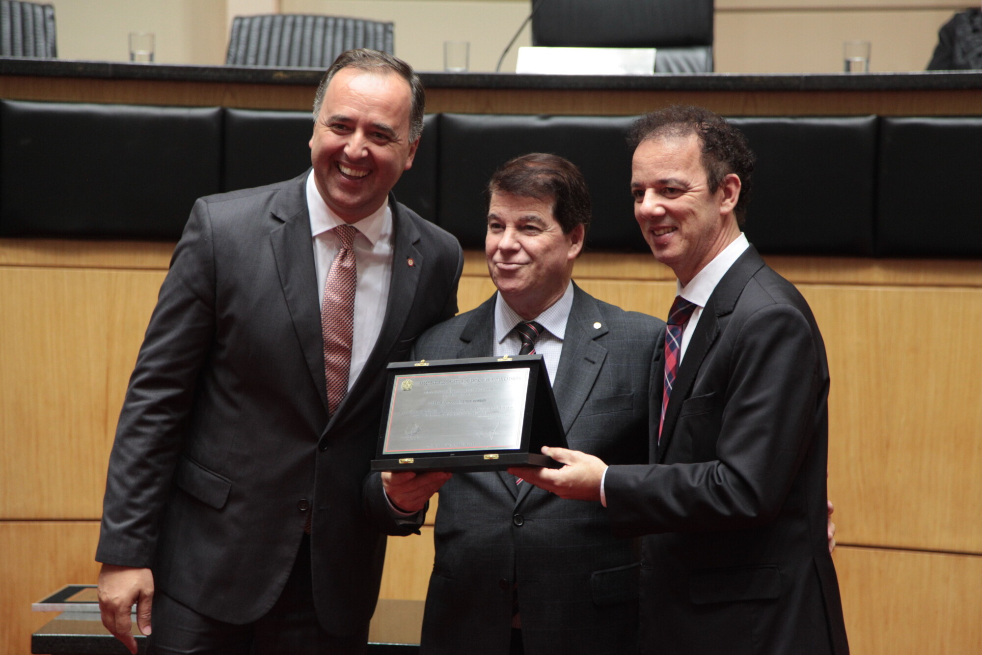 Pastor Antônio Nemer Bordin recebe placa entregue pelos deputados Kennedy Nunes (E) e Ismael dos Santos (D)