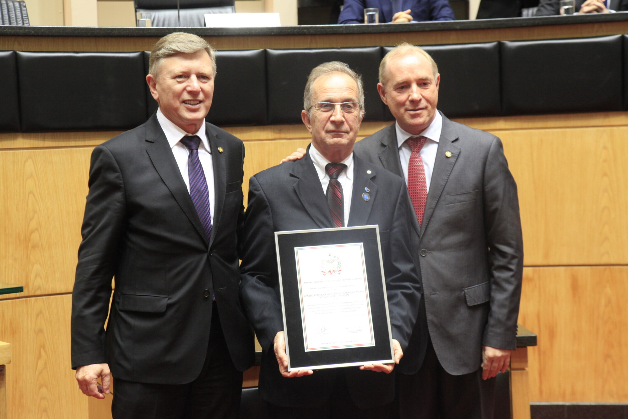 Reitor da Unidavi, Célio Martignago, recebe placa das mãos dos deputados Milton Hobus (e) e Aldo Schneider