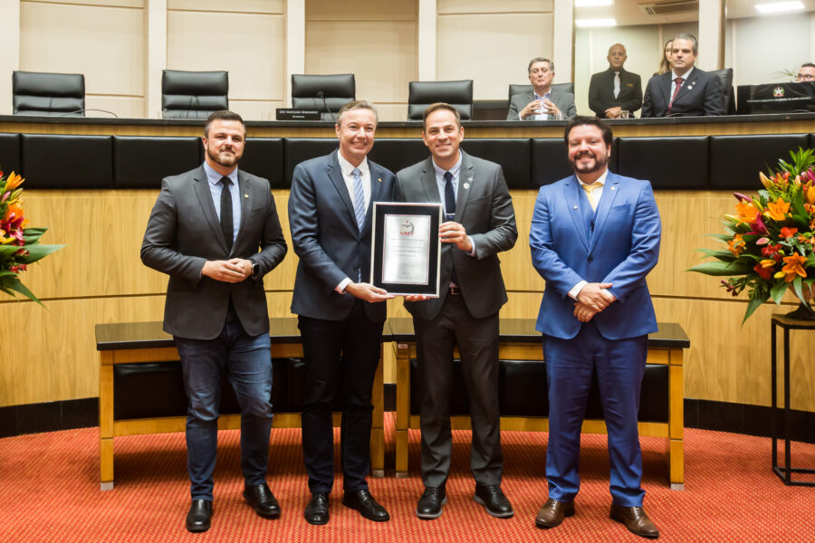 Deputado Napoleão Bernardes, ladeado pelos deputados Lucas Neves (Podemos) e Alex Brasil (PL), entrega homenagem a Célio Antônio Bernardi Júnior.