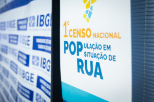 Painel com a identidade visual do 1º Censo Nacional da População em Situação de Rua ao lado de fundo com logotipos do IBGE.