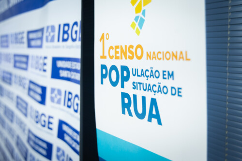 Painel com a identidade visual do 1º Censo Nacional da População em Situação de Rua ao lado de fundo com logotipos do IBGE.